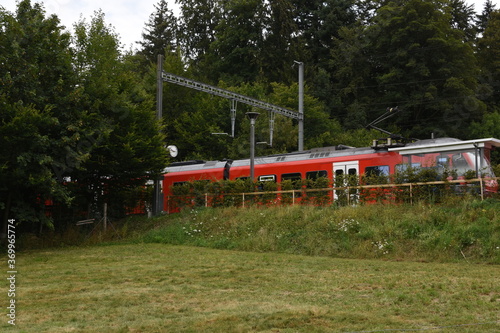 Small railway platform for passengers in local train station with red electric train heading to Uetliberg mountain in the Swiss plateau