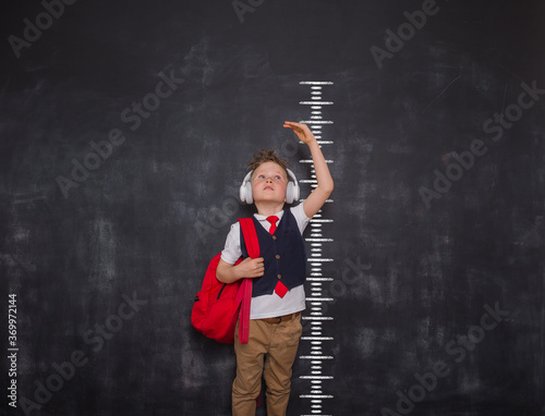Little kid boy measuring himself. School boy measuring his growth in height against a blackboard scale. Back to school