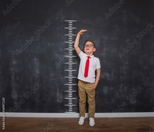 Little kid boy measuring himself. School boy measuring his growth in height against a blackboard scale. Back to school. Ready to go to school