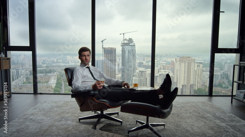 Businessman resting on chair in modern interior. Male worker drinking whiskey