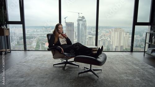 Businesswoman relaxing on chair in office. Woman smelling aroma of wine in glass