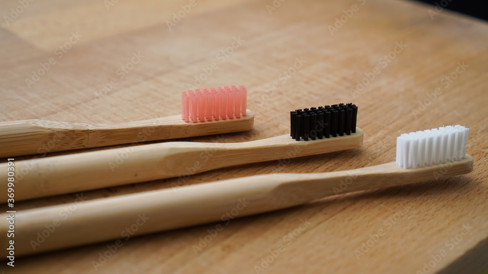 Pink, black and white color of eco-friendly bamboo toothbrushes on a wood background. Natural organic dental concept