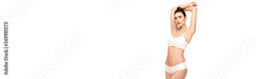 panoramic crop of woman in panties and top standing with hands above head and looking at camera isolated on white