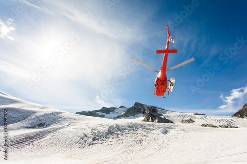A helicopter flying on a sunny day in glacier covered mountains