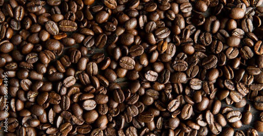 Fototapeta premium Roasted arabica coffee beans scattered on a wooden table. Fresh coffee beans.