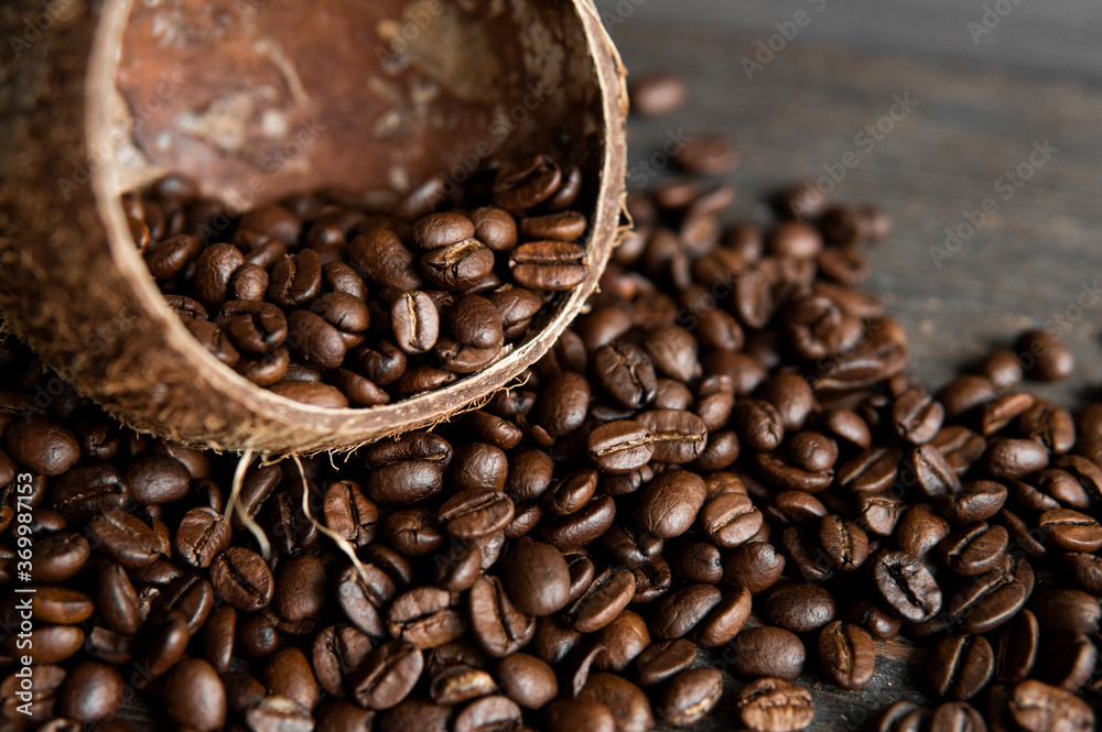Fototapeta premium Roasted arabica coffee beans scattered on a wooden table from a coconut. Fresh coffee beans.