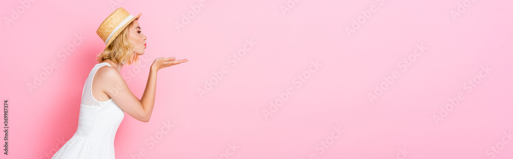 side view of woman straw hat and dress sending air kiss on pink, panoramic crop side view of woman straw hat and dress sending air kiss on pink, panoramic crop
