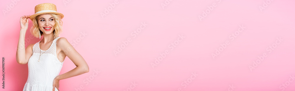 panoramic concept of woman touching straw hat and standing with hand on hip on pink panoramic concept of woman touching straw hat and standing with hand on hip on pink