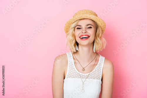 woman in straw hat laughing and looking at camera on pink