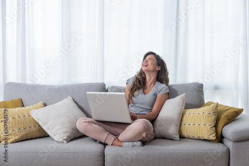 Young beautiful single woman chatting with her boyfriend or girlfriend on the laptop computer siting on the sofa and laugh with big smile