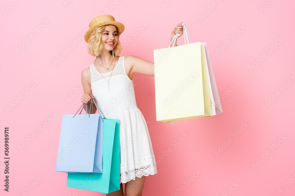 woman in straw hat looking at shopping bag on pink