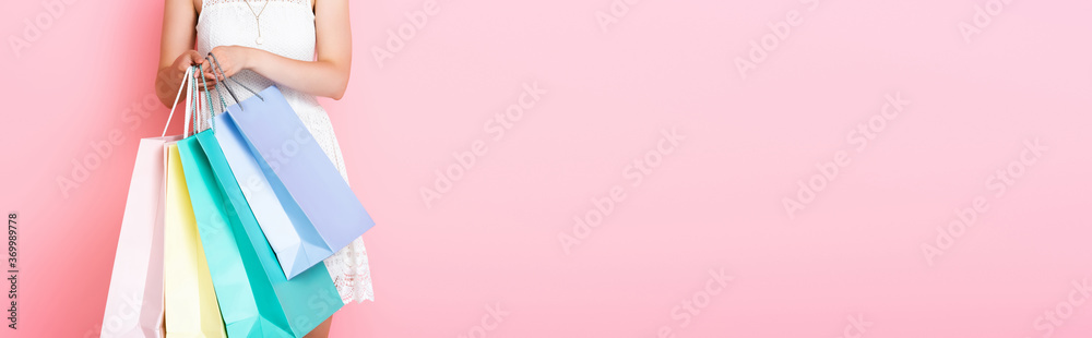panoramic crop of young woman holding shopping bags on pink