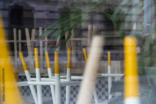 Wooden chairs and tables with yellow legs are arranged behind glass in the restaurant.