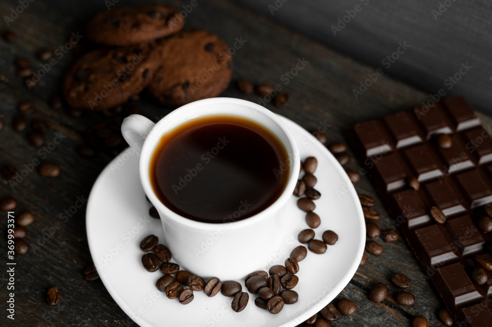 Coffee cup with cookies and chocolate on wooden table background. Mug of black coffee with chocolate cookies. Fresh coffee beans.