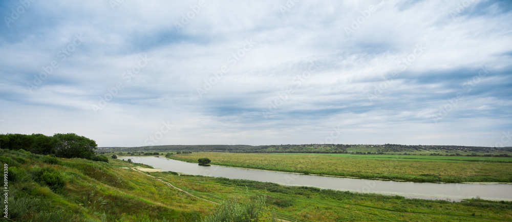 Landscape river in a bright green summer field on a cloudy day