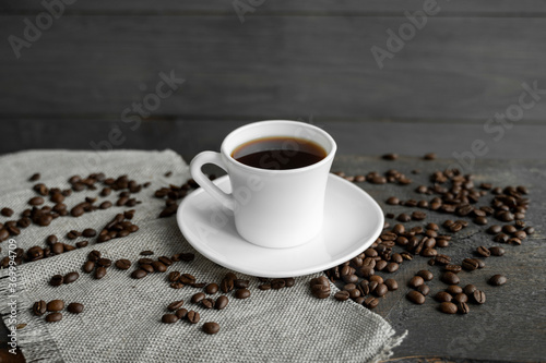 Coffee cup with roasted coffee beans on wooden table background. Mug of black coffe with scattered coffee beans on a wooden table. Fresh coffee beans.