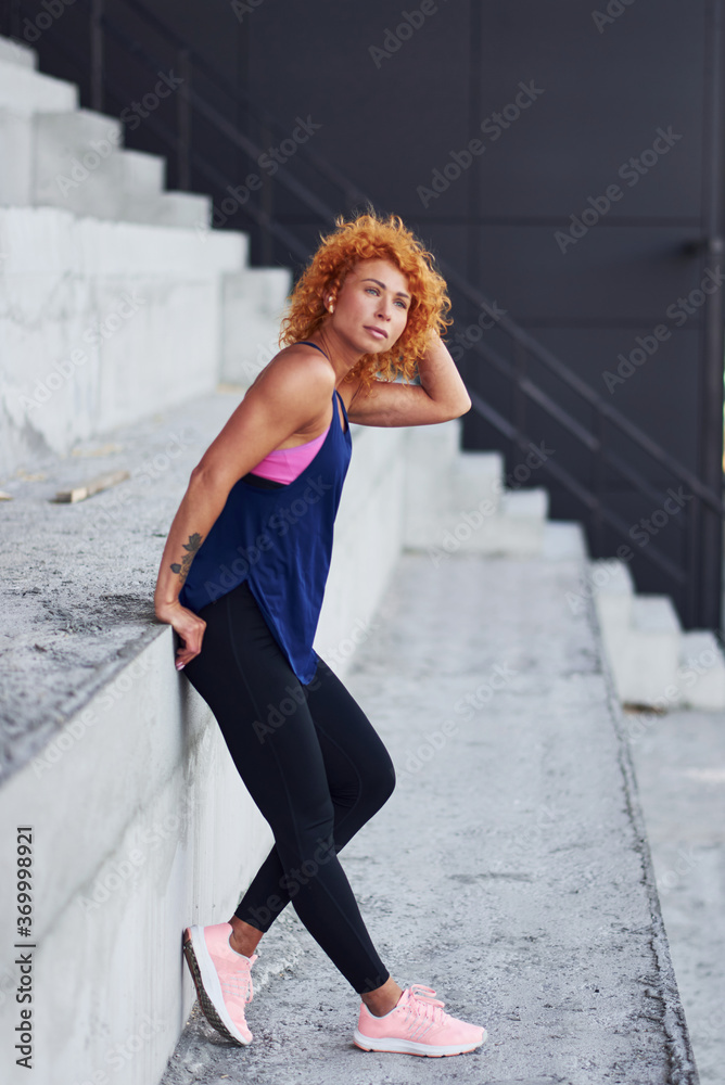 Young european redhead woman in sportive clothes standing on stairs outdoors