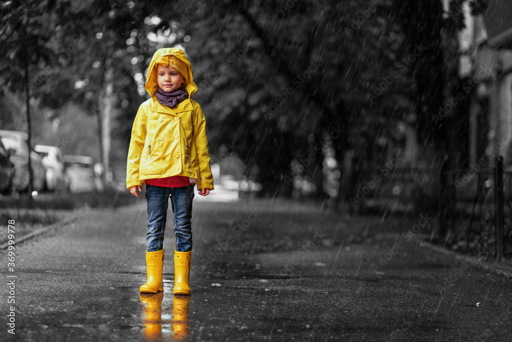 Do not be sad. child girl in yellow raincoat and rubber boots in puddle on a parking, autumn walk. Childhood happiness concept Do not be sad. child girl in yellow raincoat and rubber boots in puddle on a parking, autumn walk. Childhood happiness concept