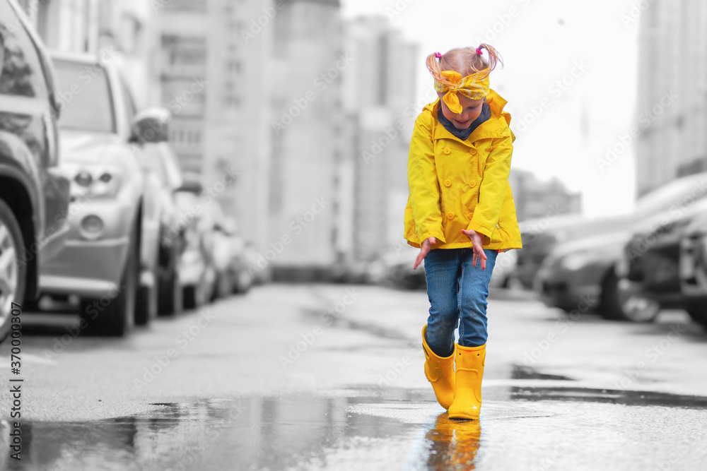 Φωτογραφία Adorable child girl in yellow raincoat and rubber boots in puddle on a parking, autumn walk
