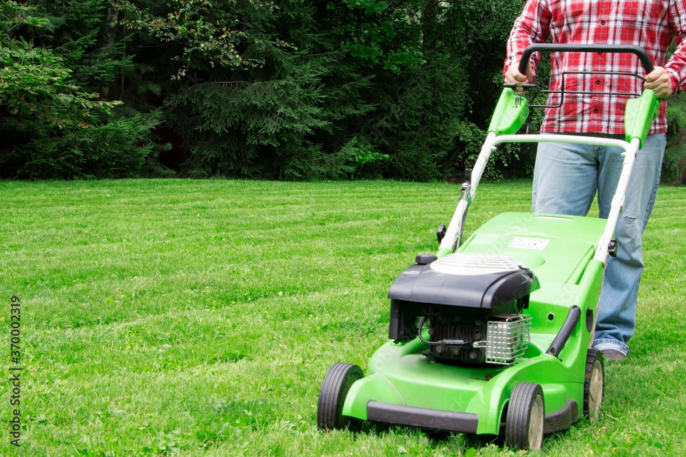 A man mowing the lawn. Cutting grass. Man working on a backyard. Man cutting grass in the garden with lawn mower A man mowing the lawn. Cutting grass. Man working on a backyard. Man cutting grass in the garden with lawn mower