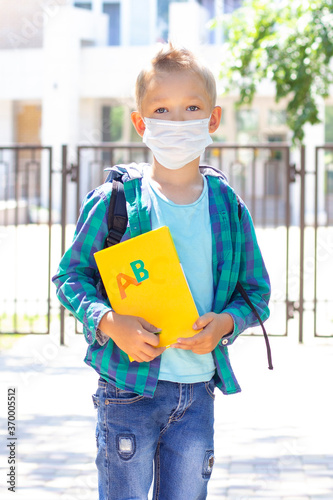 schoolboy in a protective mask with a backpack and a textbook in their hands. in a T-shirt and a plaid shirt