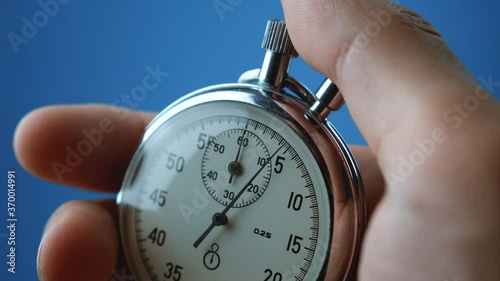 Close-up analog stopwatch in man's hand on blue background is starting and stopping