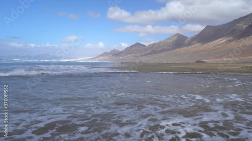 Una pareja a lo lejos juega en la orilla de la playa de Cofete con las montañas al fondo. Fuerteventura. Islas Canarias photo