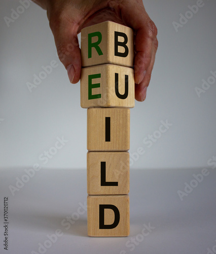 Concept word 'rebuild' on cubes on a beautiful wooden table. Male hand. White background. Business concept. Copy space.