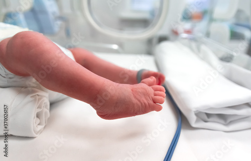 Premature baby feet with a neonatal pulse monitor, selective focus. Small newborn is placed in a premature newborn incubator. Neonatal intensive care unit