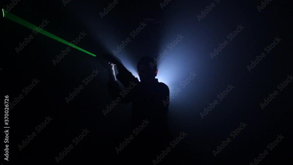 Man with green laser sword silhouetted in foggy dark room