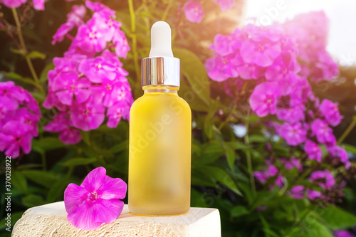 Natural essential oil in a glass bottle against a background of pink flowers. The concept of organic essences, natural cosmetic and health products. Modern apothecary.