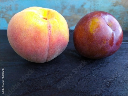 ripe peach and red plum on a black wooden table
