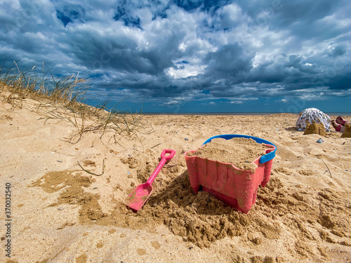Pink bucket and spade building a sandcastle on Great Yarmouth beach, Norfolk, under a cloudy summer sky