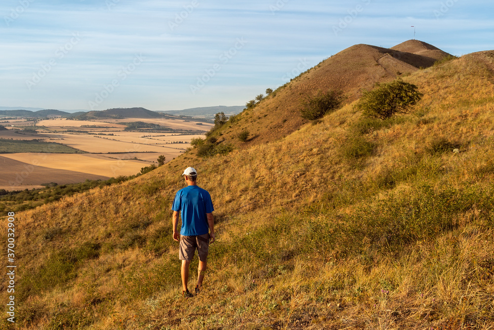 Young man walking on hill Rana and looking to Czech central mountain valley at sunrise