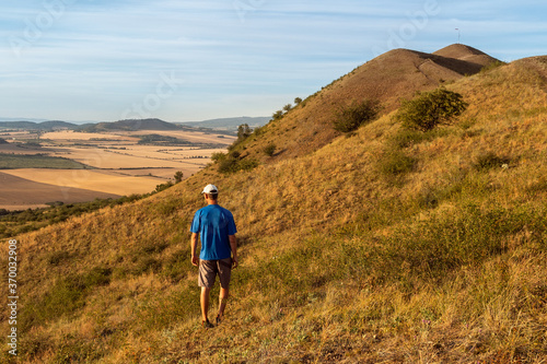 Young man walking on hill Rana and looking to Czech central mountain valley at sunrise