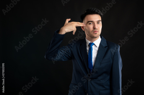 Portrait of business man wearing blue business suit and tie showing shoot in the head gesture