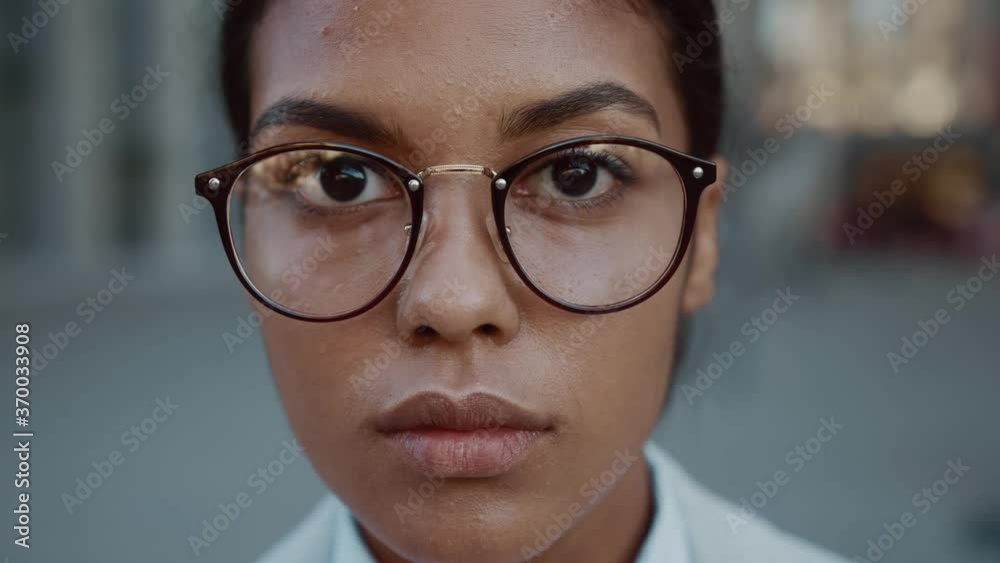 Close up face mixed race business woman in glasses standing look at camera serious outdoor in jacket posing at modern street success stylish exterior slow motion Close up face mixed race business woman in glasses standing look at camera serious outdoor in jacket posing at modern street success stylish exterior slow motion