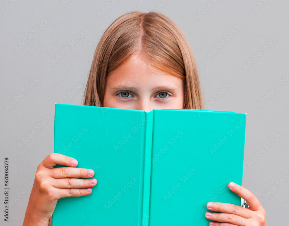Close up portrait of close cover face behind diary. Girl ready to continue reading isolated on grey background Close up portrait of close cover face behind diary. Girl ready to continue reading isolated on grey background