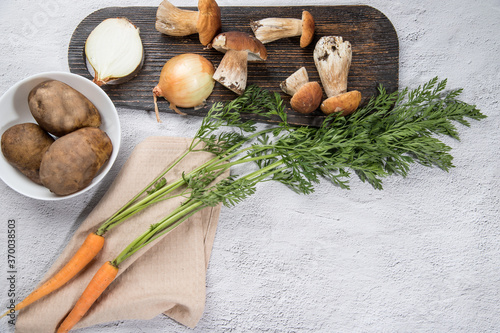 Ingredients for cooking mushroom soup-porcini mushrooms, onions, carrots, potatoes on a light background. Russian cuisine. Vertical orientation. Place for copy space