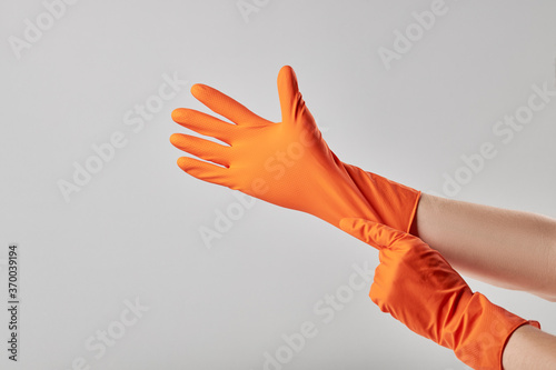 caucasian male person putting on orange washing gloves. washing and cleaning service concept. minimal. copy space. grey background. studio shot.