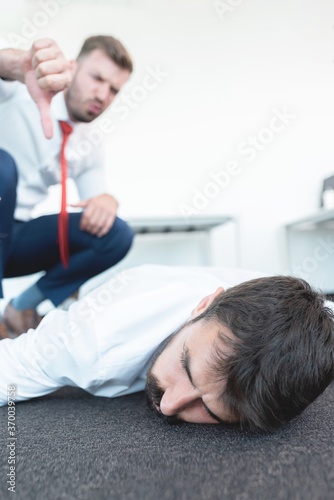 Businessman showing thumbs down gesture to exhausted coworker