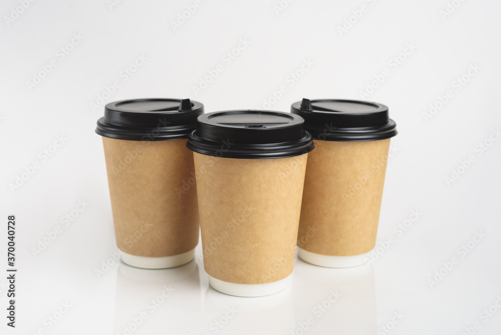 Three eco friendly paper craft cups for coffee to go with black lid on the white background. Zero waste, plastic free concept. Sustainable lifestyle. Composition with front view. Three eco friendly paper craft cups for coffee to go with black lid on the white background. Zero waste, plastic free concept. Sustainable lifestyle. Composition with front view.