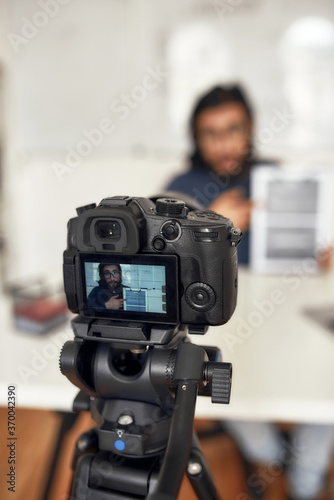 Recording video blog. Young man teaching online, explaining new theme while working from home. Focus on camera, professional digital equipment