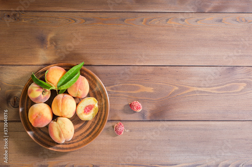 Banner with peaches on a wooden background. The peaches are on a brown clay plate. The view from the top