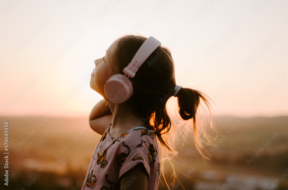Fototapeta premium Side view close up portrait of a child with pink headphones listening to music looking up