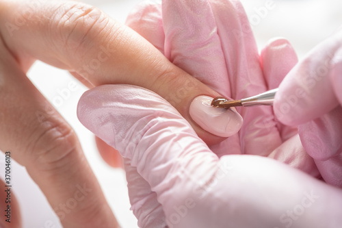 Woman in nail salon receiving manicure by beautician. Manicure process in beauty salon, close up. Close up of a woman hand with transparent nail polish after the manicure. 