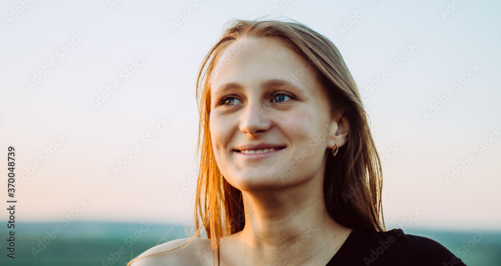 Close up front view portrait of a caucasian young woman smiling and looking to the side, against the sky Close up front view portrait of a caucasian young woman smiling and looking to the side, against the sky