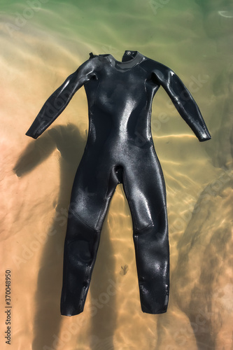 A black wetsuit floats in the water in the bright sun.