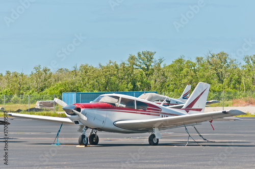 front view, close distance of a single, prop, airplane secured with tie downs, in parking tarmac, of  a tropical airport