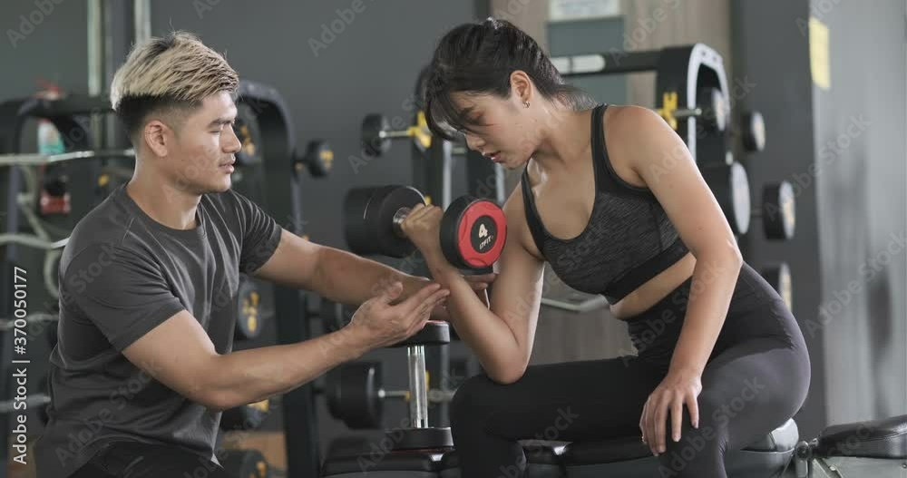 Young asian woman doing dumbbell workout on bench with personal coach. Young asian woman doing dumbbell workout on bench with personal coach.